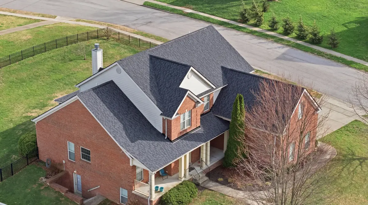 Aerial of a brick home with a charcoal shingle roof, white dormer and black fence