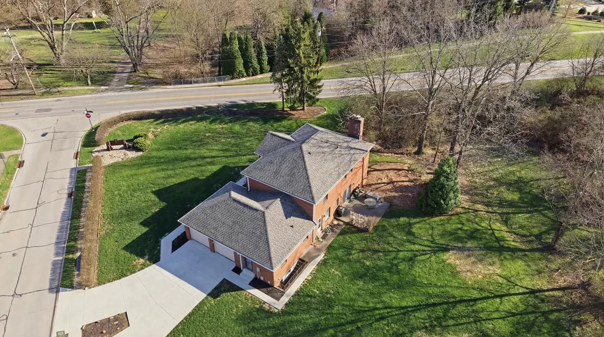 Aerial of a brick home with a grey shingle roof, wide lawn and curving walkway