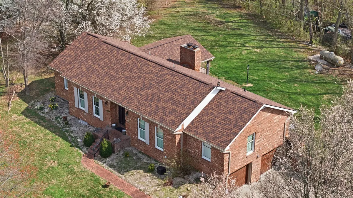 Aerial of a brick ranch with a brown shingle roof and spring trees