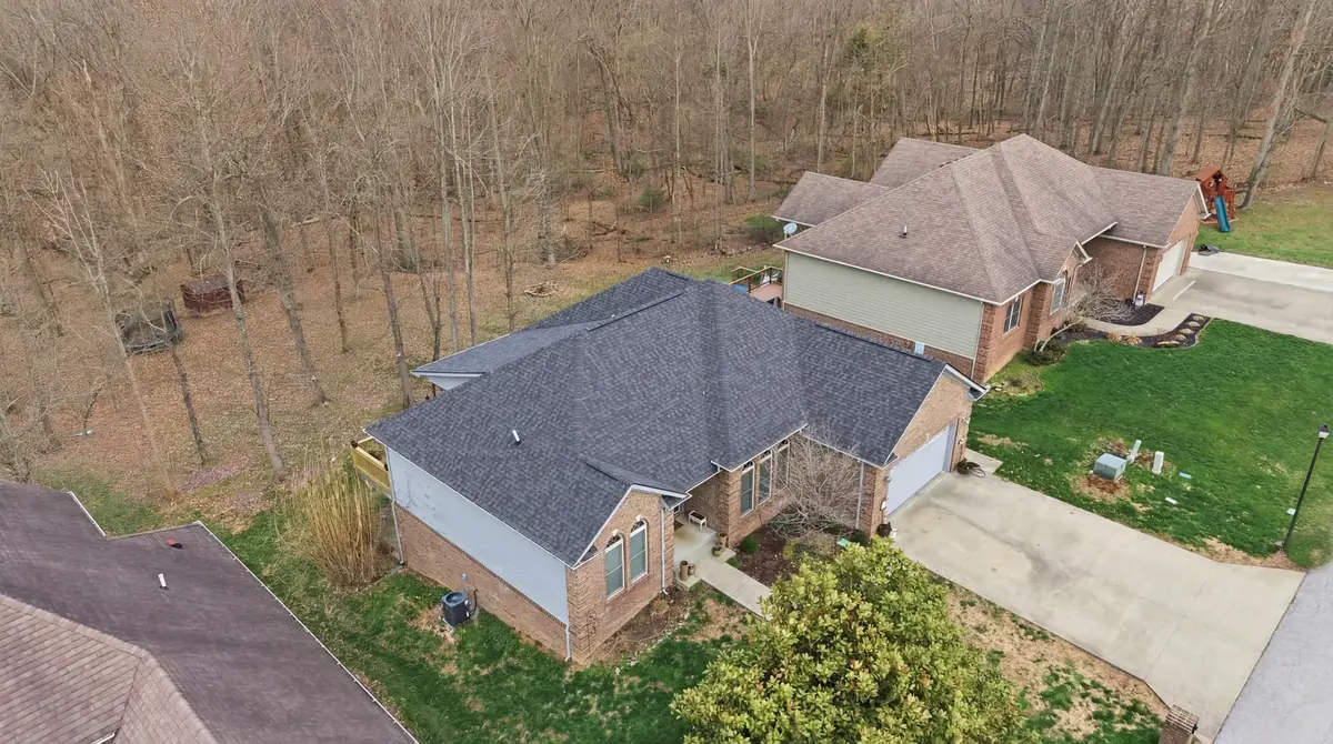 Aerial of a brick ranch with a grey shingle roof backing onto woods