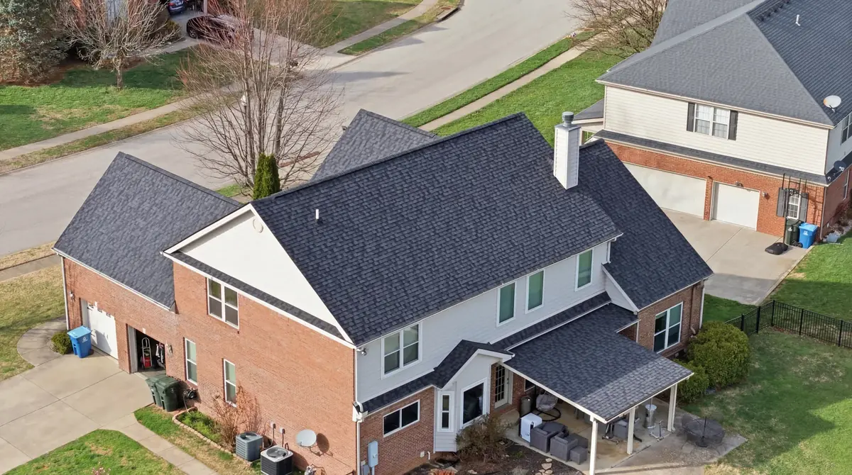 Aerial of a large brick two story with a new charcoal shingle roof and covered rear patio