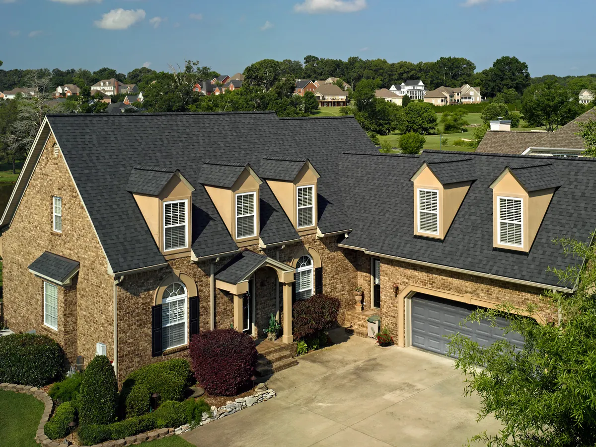 Brick home with dormer windows under a dark shingle roof