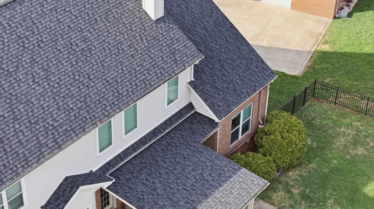 Close aerial of a dark grey shingle roof over white siding and brick
