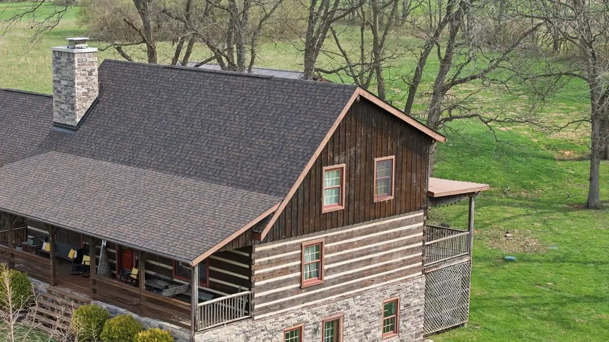 Close aerial of a two story log and stone home with a brown shingle roof