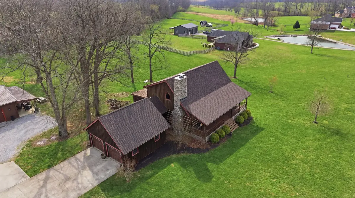 Aerial of a log home with a brown shingle roof on open pasture with a pond