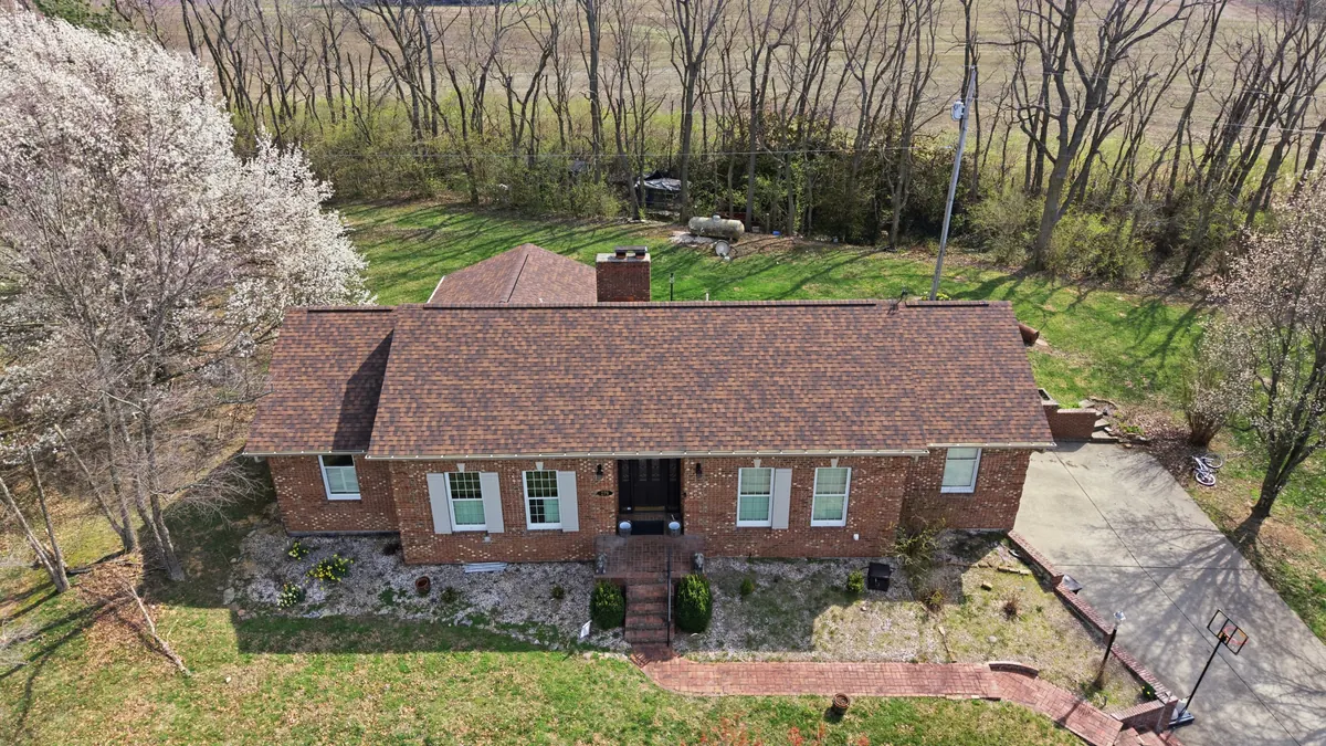 Aerial view of a long brick ranch home with a new roof and a blossoming tree